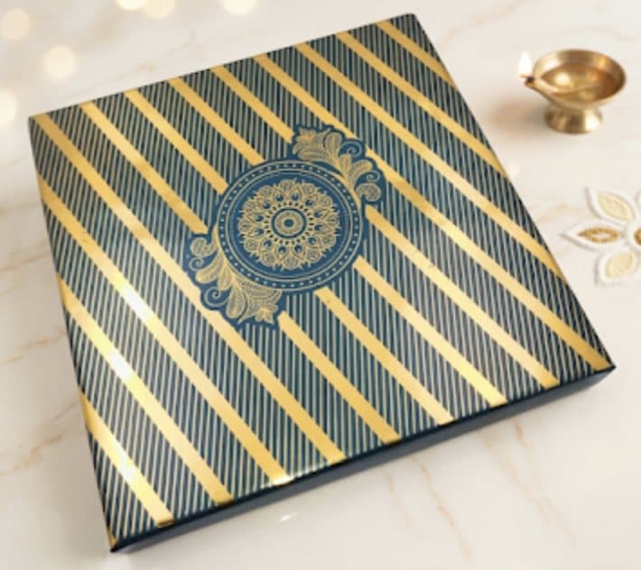 Navy and gold striped Diwali gift box beside a diya